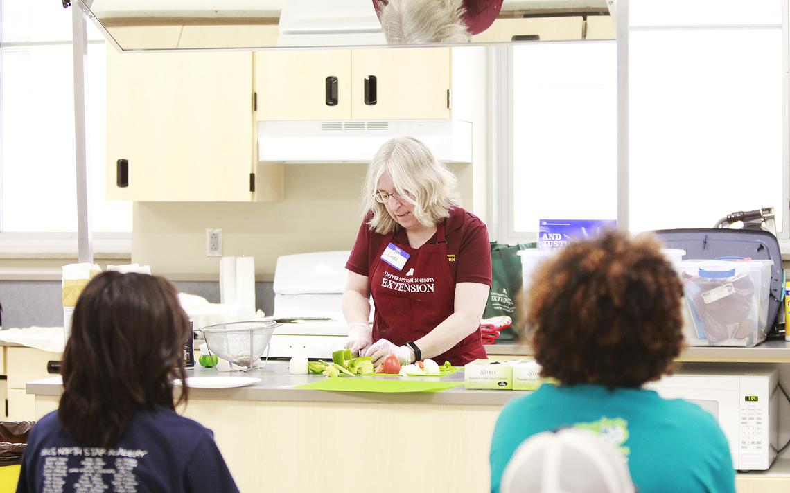 Long time University of Minnesota Extension employee, Linda Erdahl , demonstrates how to properly cut vegetables for their pizza. When she is done the students break into their groups and work on their pizzas. Jamie Lund/Pine Journal