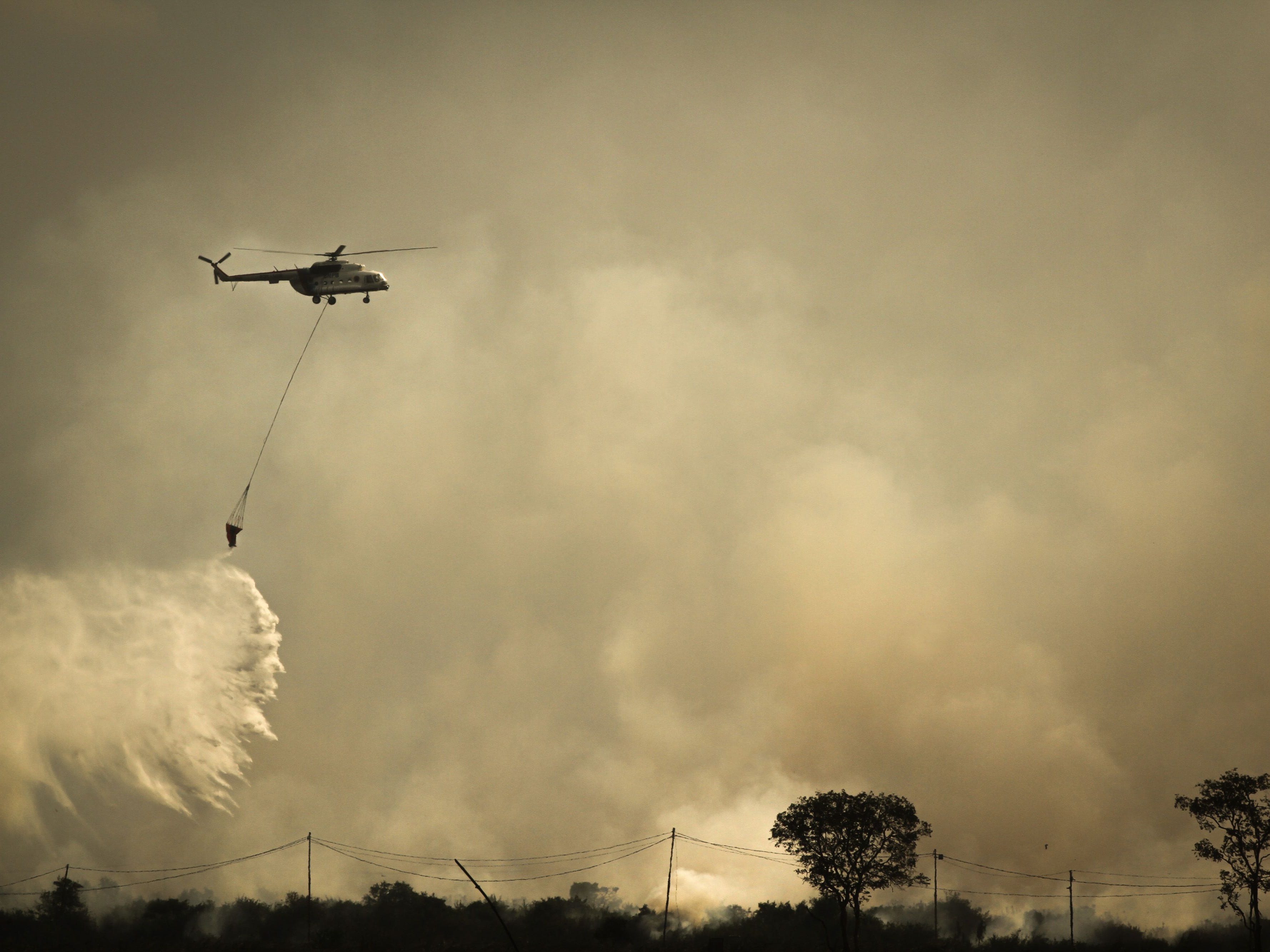 A helicopter releases a bucket of water to extinguish a fire in a peatland forest in Ogan Ilir district in South Sumatra on Aug. 3, 2019.