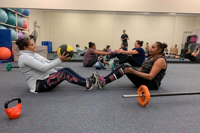 Moorundie Ruwe Ninkawi members exercise A group of women are sitting on the floor, passing medicine balls to each other. Their feet are touching.