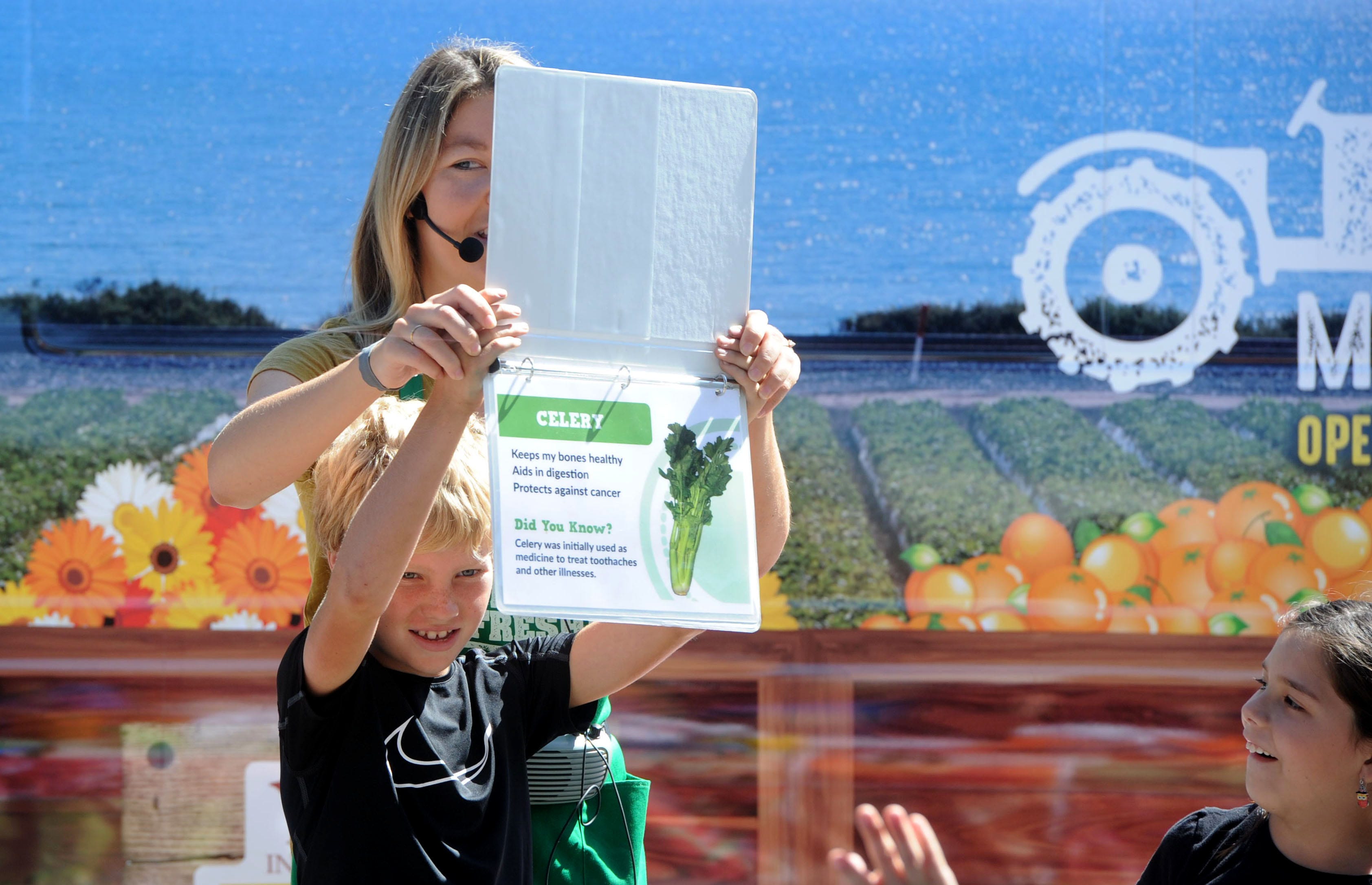 Emily Skaar helps Bryce Daw hold up a celery picture to show other third-graders at Mound School when Students for Eco-Education and Agriculture’s 30-foot Farm Fresh van came to visit.