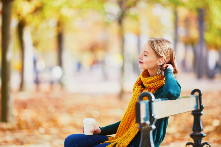 Woman drinking coffee on park bench in the fall