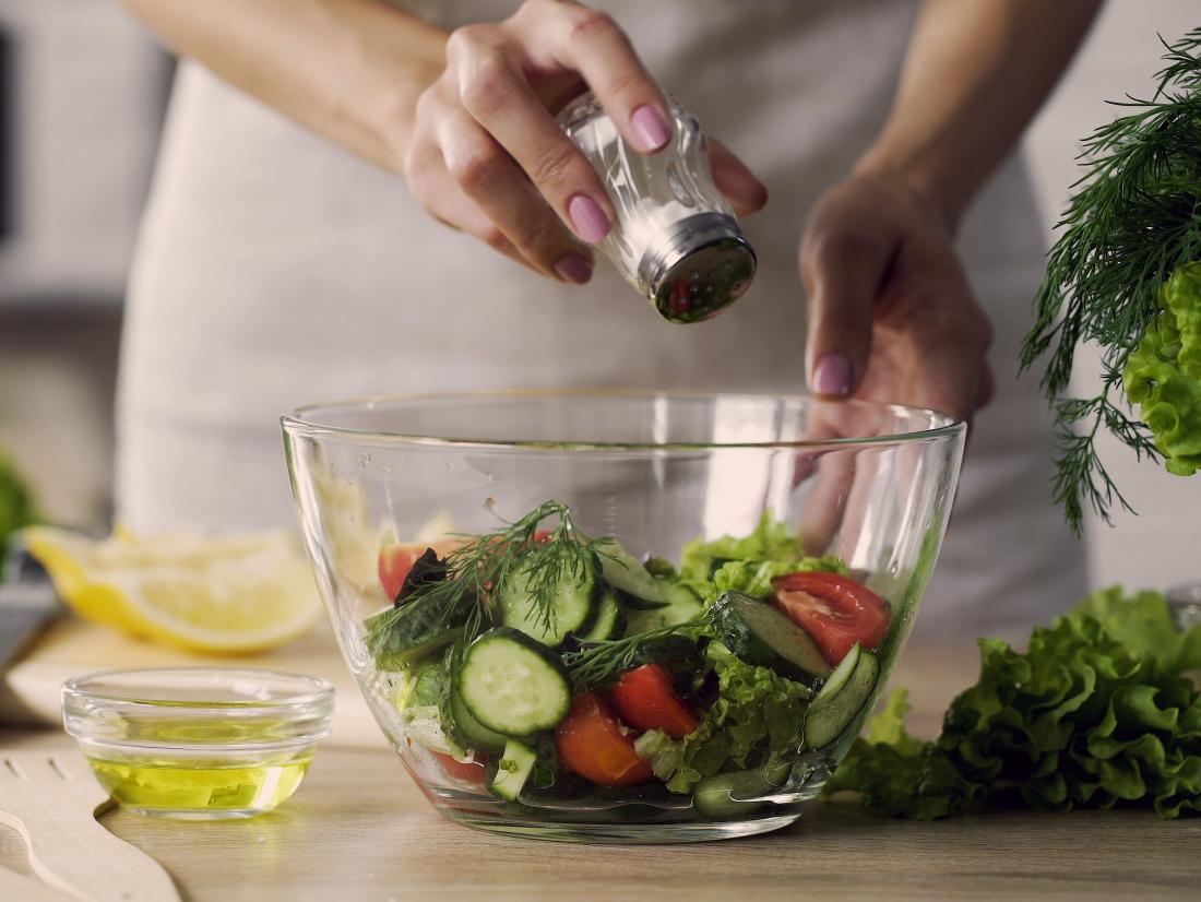 a woman adding salt to a salad.