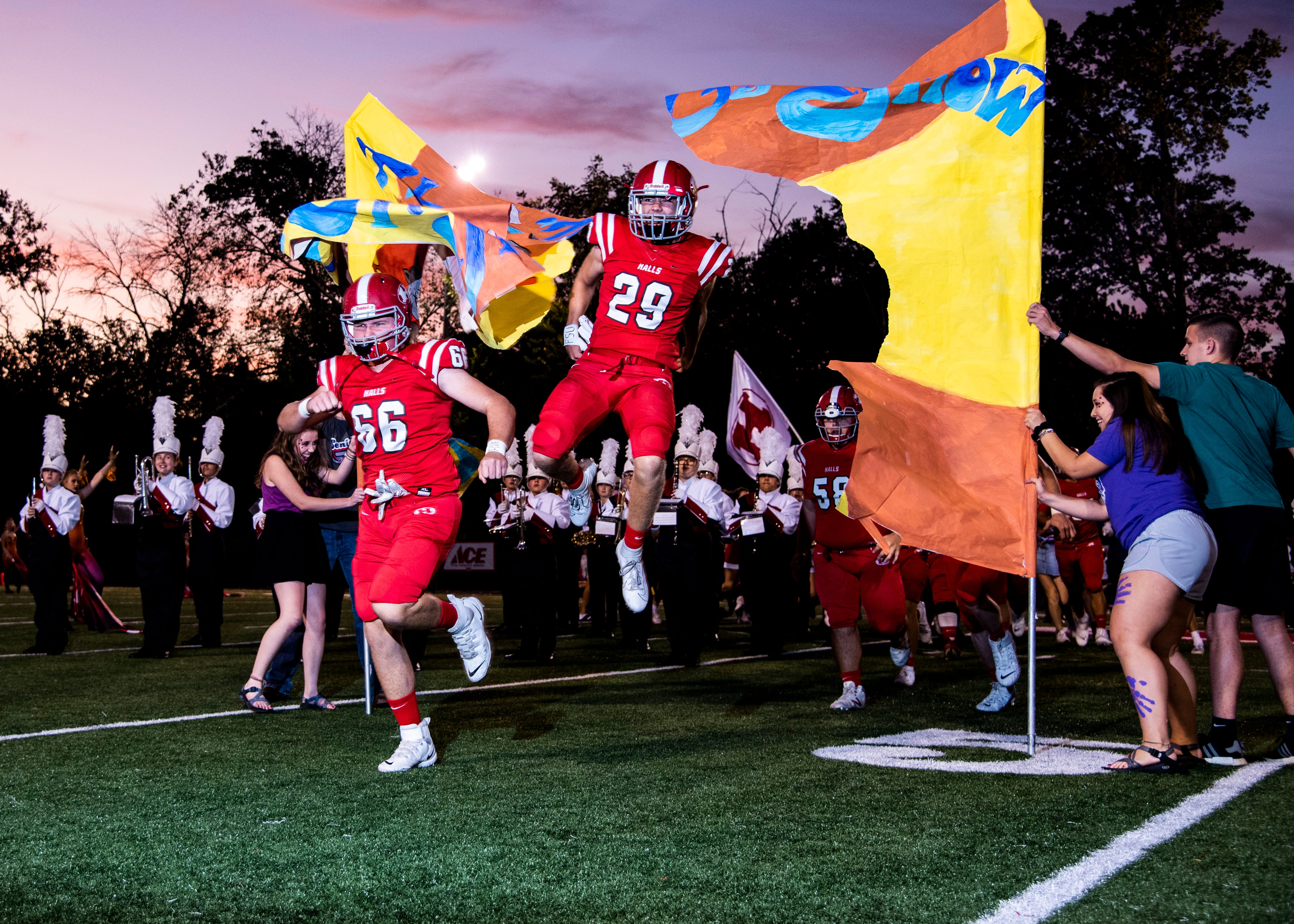 Halls' Jacob Williams (66) and Parker Breeden (29) jump through a spirit banner before the Halls and Central high school football game on Friday, October 4, 2019 at Halls High School.