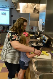 A parent helps her child chop and cook vegetables for a healthy meal.