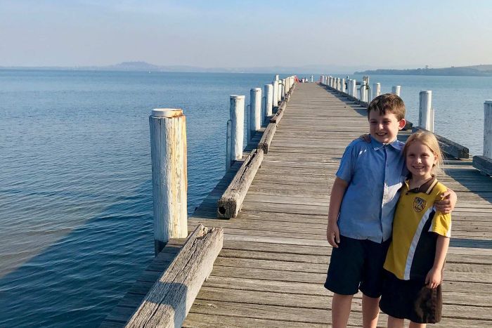 two children stand on a pier surrounded by ocean