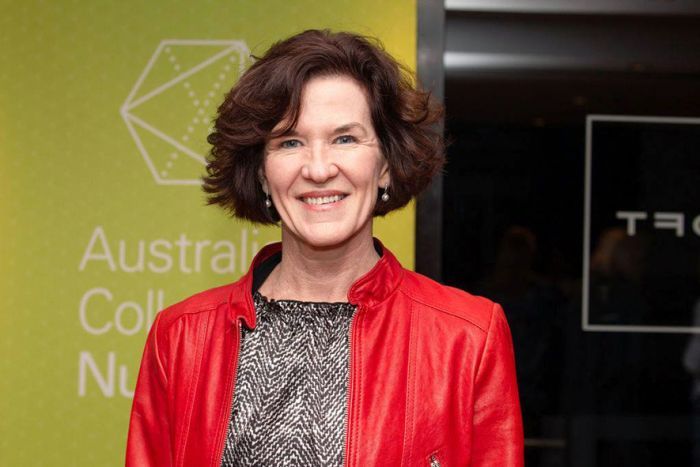 Professor Jeanine Young A middle aged woman with short brown hair stands in a red jacket in front of a green sign.