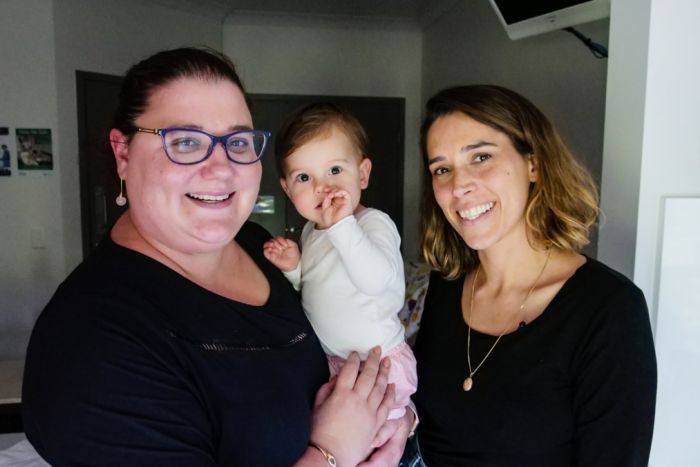 Two women smile. One is holding a baby.