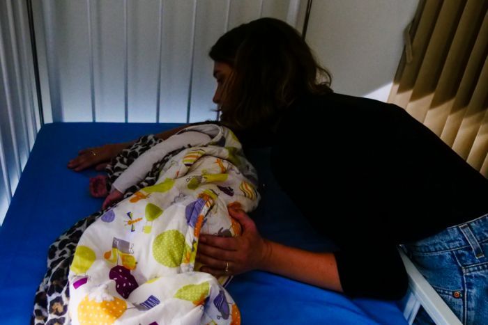 A young mum pats her baby to sleep in a cot.