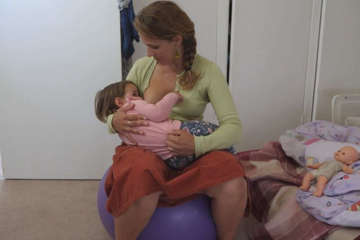 A mother sitting on an exercise ball, looking down on her breastfeeding baby.