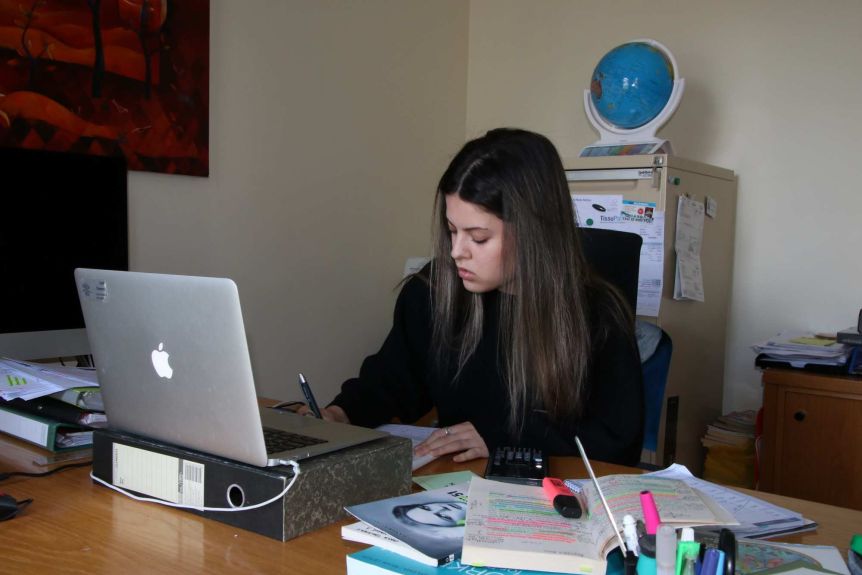 A young woman sits at a desk studying with a laptop in front of her.