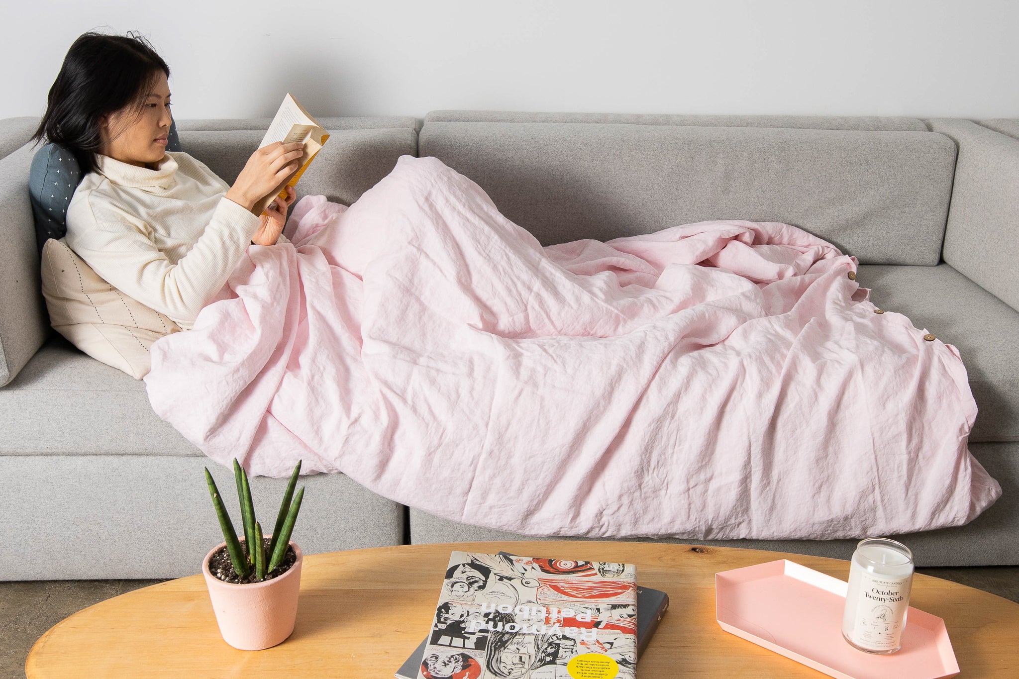 A person reading a book on a sofa, while using a weighted blanket.